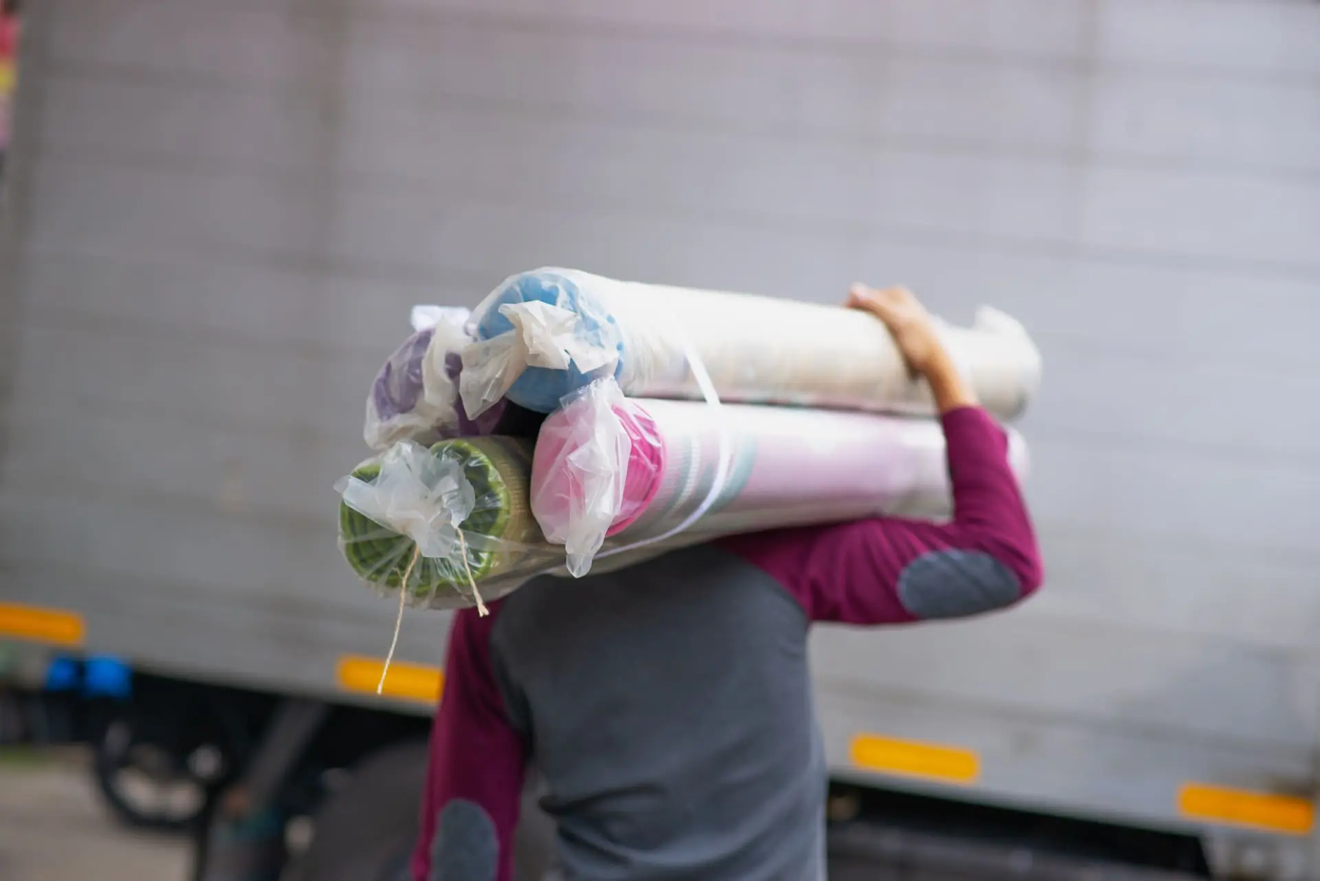 Homme en train de porter sur son épaule droite des rouleaux de textile